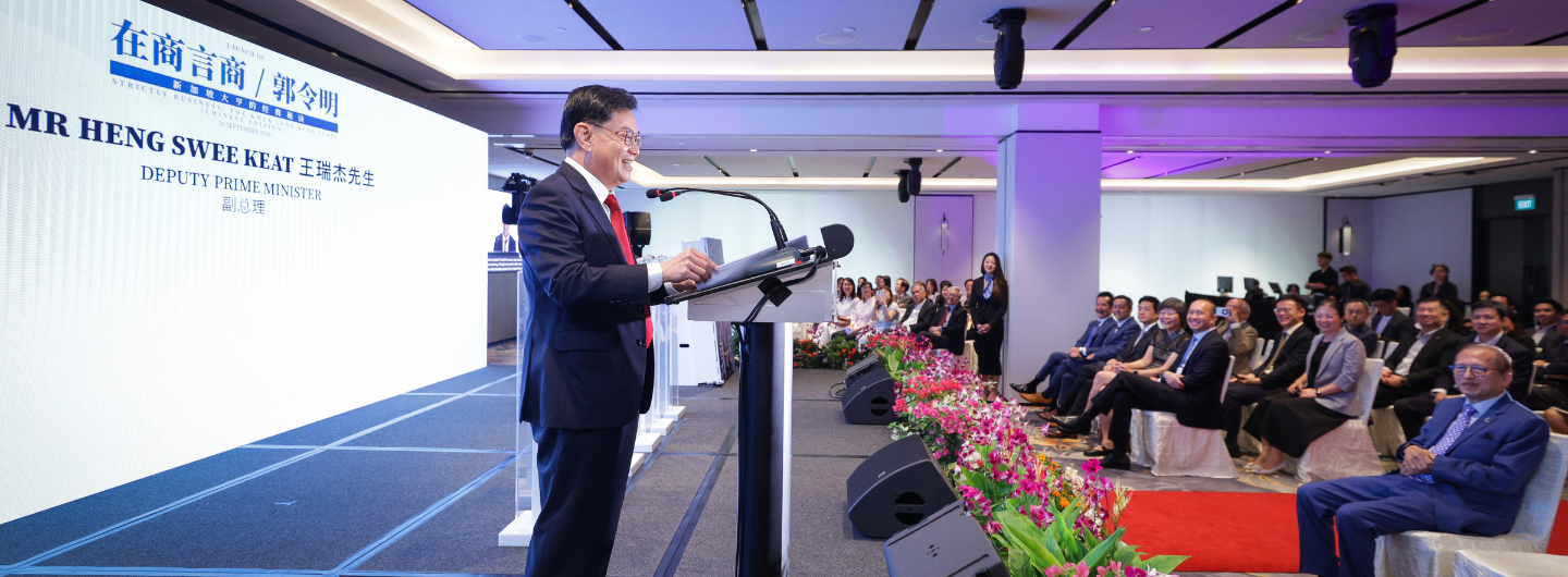 Heng Swee Keat at podium, speaking to audience seated on red carpet in large room.